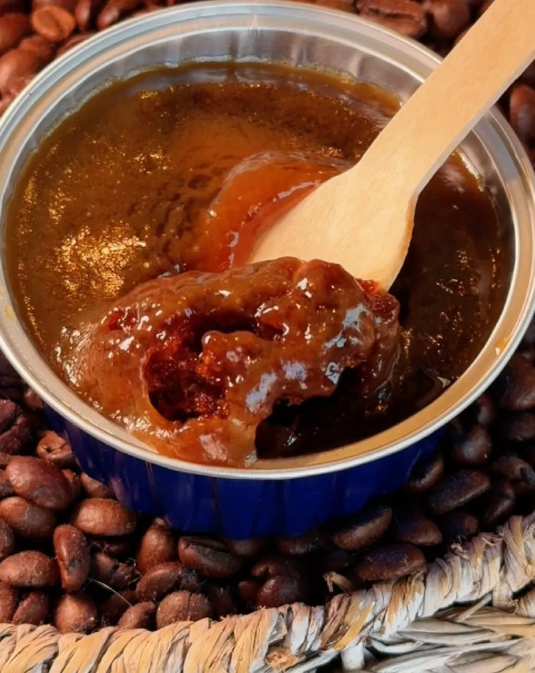 Date pudding in a blue foil cup with a wooden spoon, on coffee beans