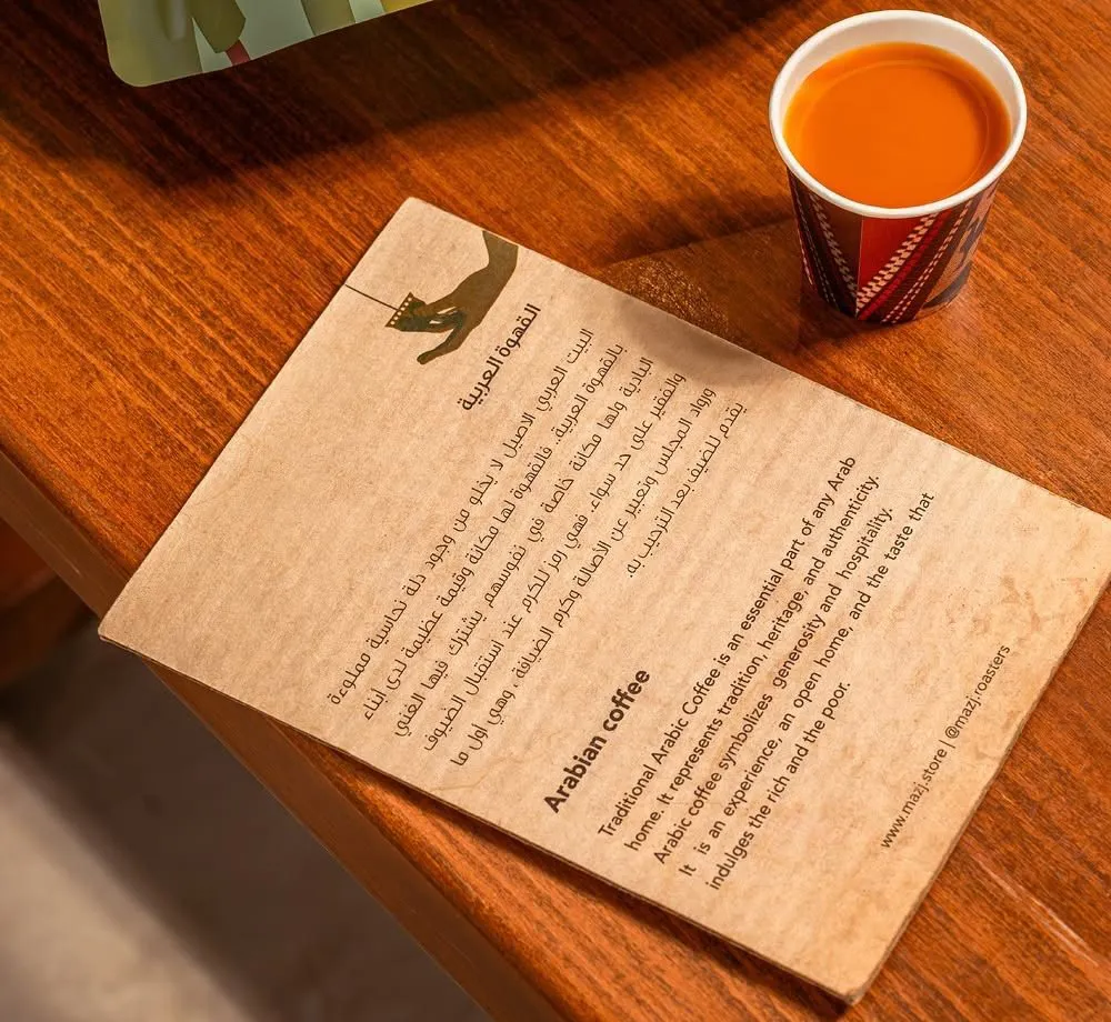 A Mazj Arabic coffee card and a small cup of Arabic coffee on a wooden bench