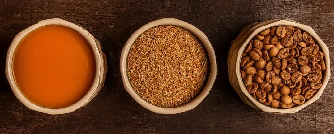 Three ceramic bowls holding brewed Arabic coffee, the ground blend and whole beans